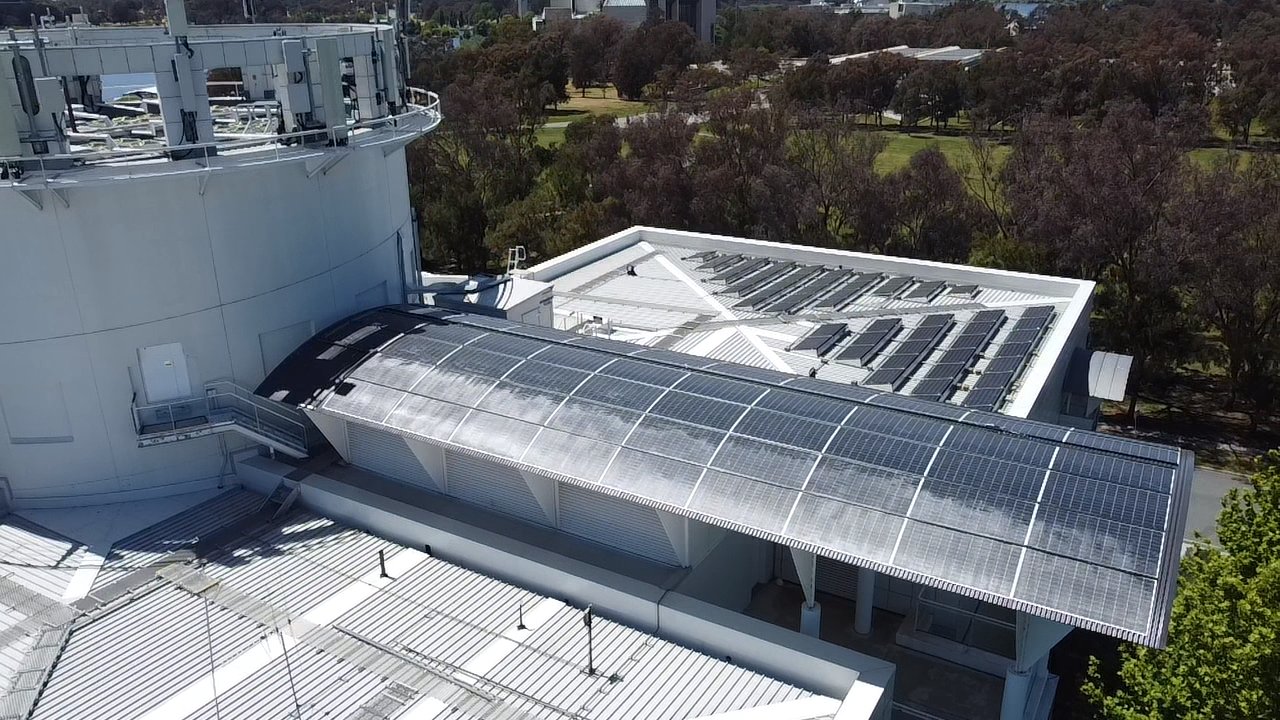 Aerial view of the white Questacon building with a curved solar canopy and a tilted array on the flat roof beyond