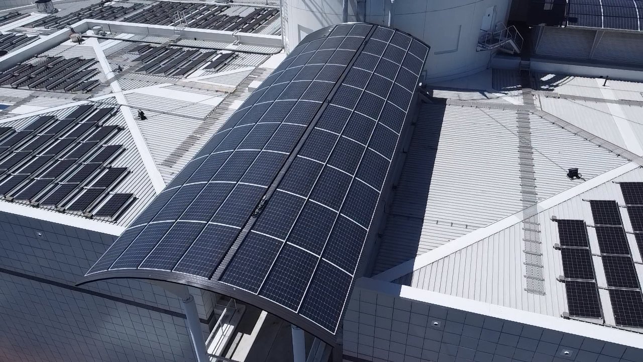 Overhead of a barrel-vault solar canopy and surrounding rooftop arrays on the square-tiled Questacon facade